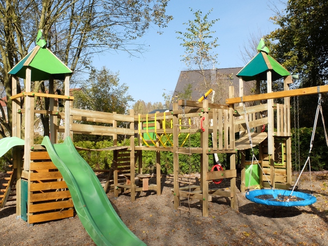 Großer hofeigener Spielplatz mit Rutschen, Schaukeln, Kletterturm und verschiedenen Spielbereichen, wie Kaufmannsladen, Auto, Kleinkindertisch